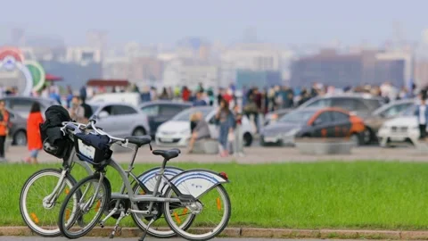 Two bikes parked near grassplot and road with crowd of people near cars Stock Footage 276375290