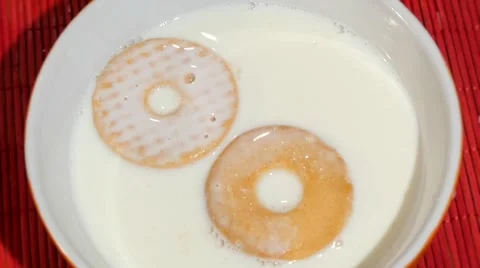 Two biscuits falling into a bowl full of fresh milk Видео 41393689