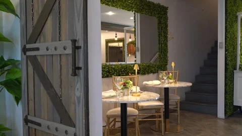 Two bistro tables by a hedge-framed mirror beside a staircase Stock Footage 345554776