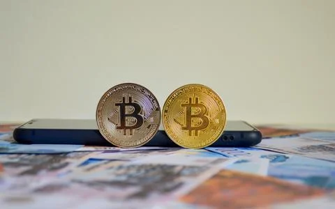 Two Bitcoin coins against a backdrop of Russian rubles Stock Photos