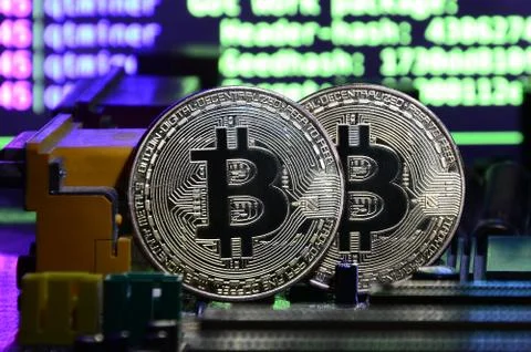 Two bitcoins lies on a videocard surface with background of screen display of Stock-Fotos