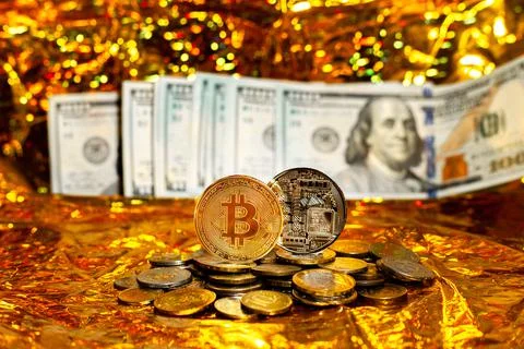 Two bitcoins on a stack of coins against a background of hundred-dollar bills Stock Photos