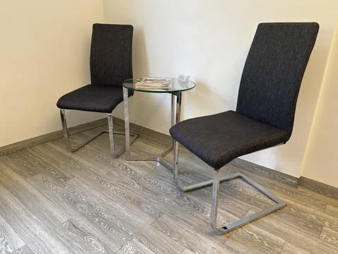 Two black chairs and a small round glass table with metal legs stand in the.. Stock Photos