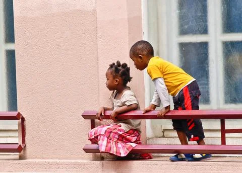 Two black children on window ledge exterior of building side view looking at  Foto stock