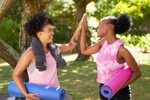Two Black friends high five in the park after doing yoga, with mats and towels Stock Photos