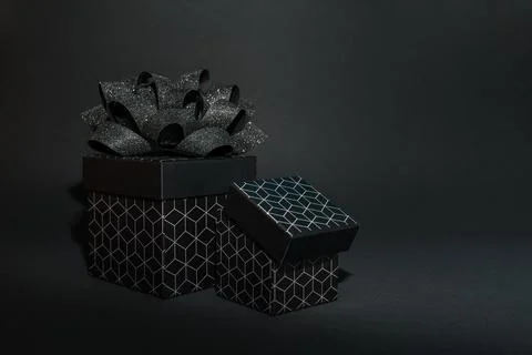 Two black gift box with a geometric pattern and a black bow on a black back.. Stock Photos