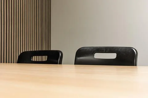 Two black plastic chairs behind wooden table in modern meeting room Fotos Stock