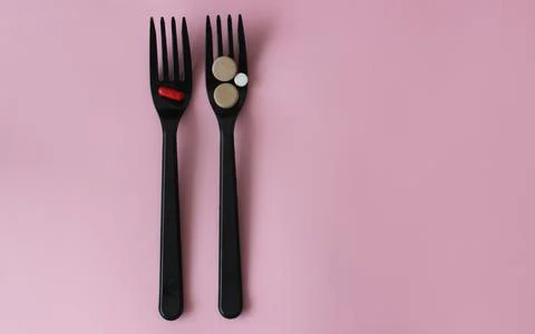 Two black plastic forks with colored tablets on a pink background. Stock Photos
