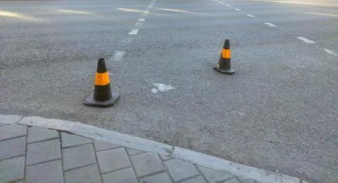 Two black traffic cones with orange reflective stripes stand on an asphalt .. Stock Photos
