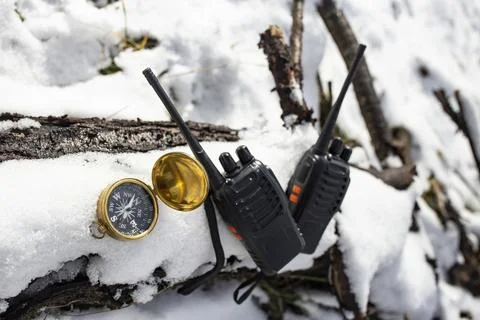 Two black walkie talkies on a tree log covered in frozen white snow next to.. Stock Photos