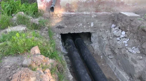 Two black water heating pipes in ditch going inside house Video stock 55859068