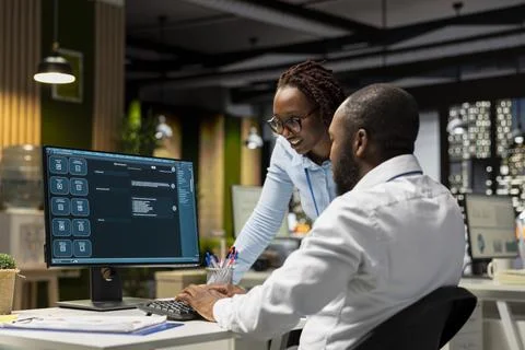 Two black workers interacting with a virtual assistant on computer at desk Stock Photos