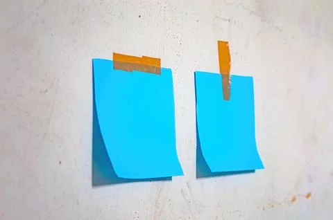 Two blank blue sticky notes taped to a textured white wall with brown tape,.. Stock-Fotos