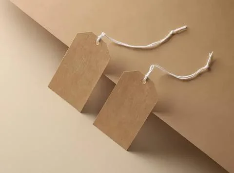 Two blank brown tags hanging on white strings on beige background Stock Photos