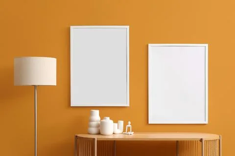 Two blank white picture frames on a vibrant orange wall above a wooden consol Фото