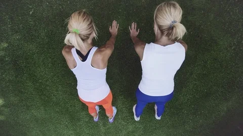 Two blonde twins in white t-shirts doing sports exercises on the green grass Stock Footage 119489265