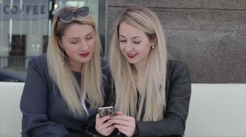 Two blondes are sitting in a café and discuss photos in the smartphone Vídeo Stock 64220925
