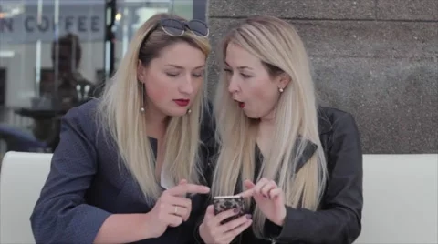 Two blondes are sitting in a café and discuss photos in the smartphone Vídeos de archivo 64221064