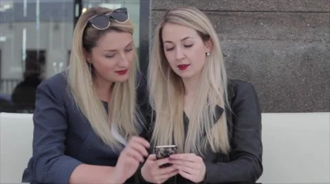 Two blondes are sitting in a café and discuss photos in the smartphone Vídeos de archivo 64221305