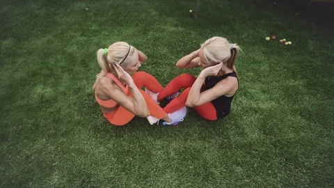 Two blondes, twin sisters, do sports exercises on the green grass Stock Footage 120838011
