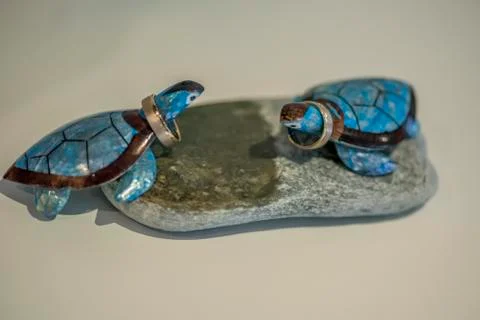 Two blue cheramic turtles on round stone decoration holding wedding rings. Stock Photos