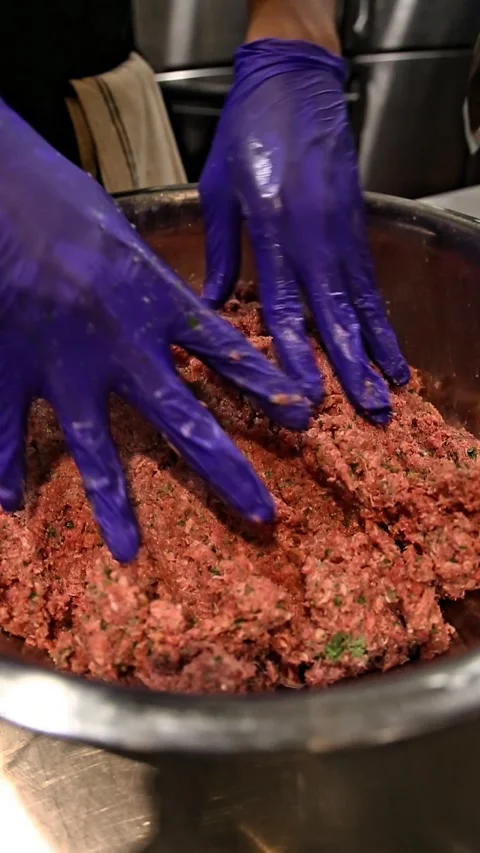 Two blue-gloved hands mixing ground meat in a stainless steel bowl 動画素材 310823421
