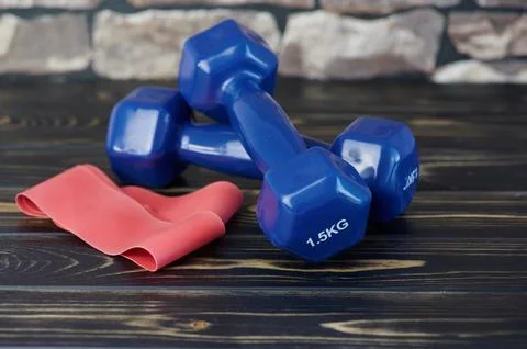 Two blue hand weights beside a red elastic exercise band against wooden bac.. Stock Photos