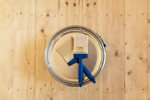 Two blue-handled paintbrushes on the lid of a paint can on a wooden floor, 写真素材