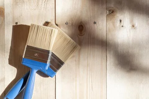 Two blue-handled paintbrushes on a light wooden floor, symbolizing preparatio Stock-Fotos