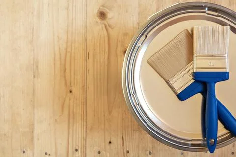 Two blue-handled paintbrushes on a paint can lid against a wooden texture, Foto stock
