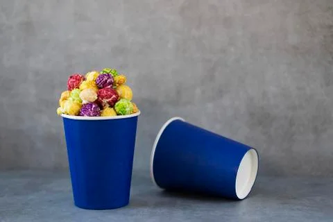Two blue paper cups with multi-colored caramel popcorn on gray background. Stock Photos