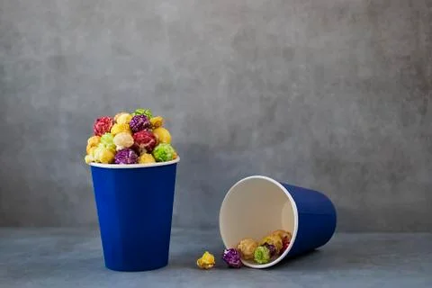 Two blue paper cups with multi-colored caramel popcorn on gray background. Stock Photos