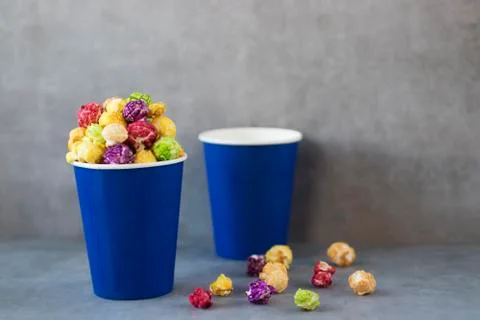 Two blue paper cups with multi-colored caramel popcorn on gray background. Stock Photos