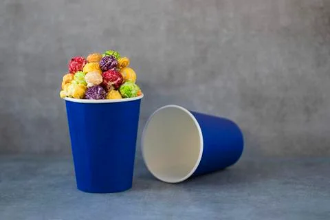 Two blue paper cups with multi-colored caramel popcorn on gray background. Stock Photos