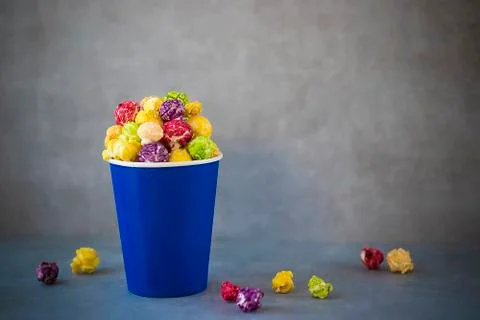 Two blue paper cups with multi-colored caramel popcorn on gray background. Stock Photos