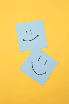 Two blue sticky notes with smiley faces on yellow background Stock Photos