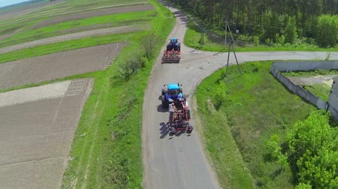 Two blue tractor with trailers driving down the road near the field. Aerial. Video stock 37669939