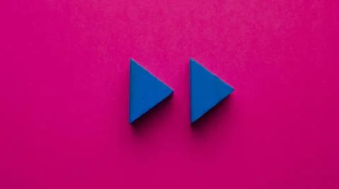 Two blue wooden triangles simulating the play icon on a pink background Stock Photos
