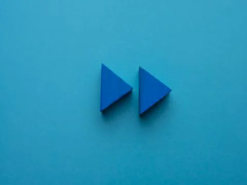 Two blue wooden triangles simulating the play icon on a blue background Stock Photos