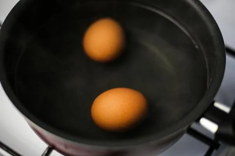 Two boiled brown eggs in a pot of boiling water Stock Photos