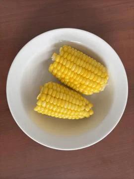 Two boiled corn cobs served in a white bowl Stock Photos