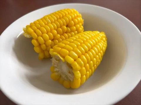 Two boiled corn cobs served in a white bowl Stock Photos