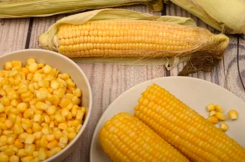 Two boiled ears of corn, corn kernels and untreated ears of corn on a wooden  Stock Photos