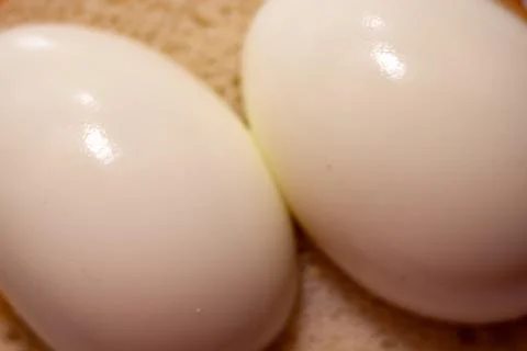 Two boiled eggs in white shells resting on a textured light brown surface Stock-Fotos