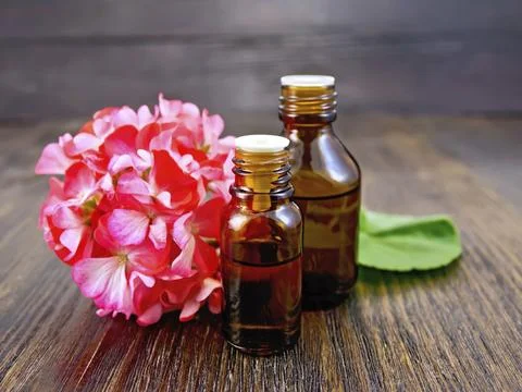 Two bottle of oil with green leaf and flower of pink geranium on a wooden boards Stock Photos