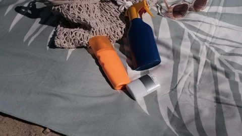 Two bottles and a stick of sunscreen fall onto a patterned beach towel in slow 스톡 동영상 313290645