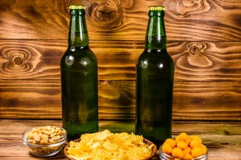 Two bottles of beer and different snacks on wooden table Stock Photos
