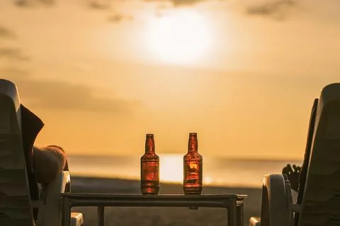 Two bottles of beer are on the table at sunset on the beach - Two friends o.. Stock Photos