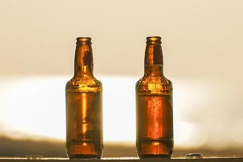 Two bottles of beer at sunset on a table on the beach in close-up. The concept Stock Photos