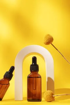Two bottles different size with serum in arch with floral extracts craspedia Stock Photos